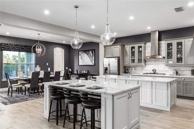 kitchen featuring a large island, wall chimney range hood, pendant lighting, appliances with stainless steel finishes, and gray cabinetry