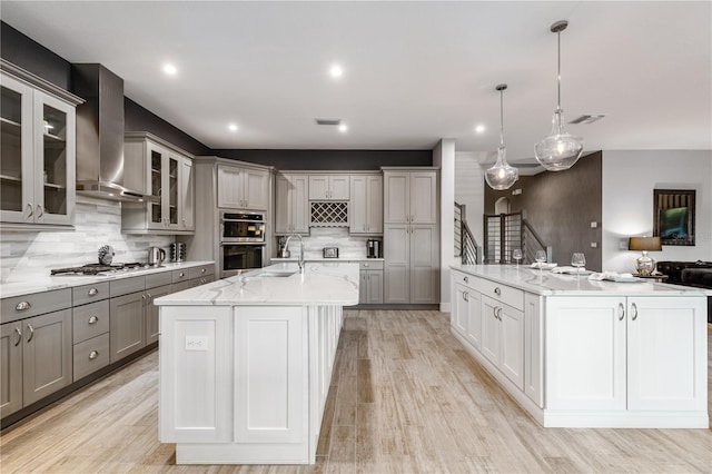 kitchen with wall chimney exhaust hood, stainless steel appliances, hanging light fixtures, and a large island with sink