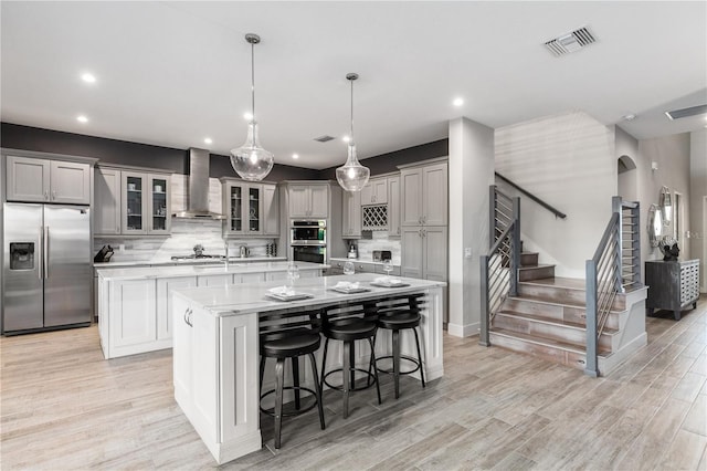 kitchen featuring gray cabinets, appliances with stainless steel finishes, hanging light fixtures, a spacious island, and wall chimney exhaust hood