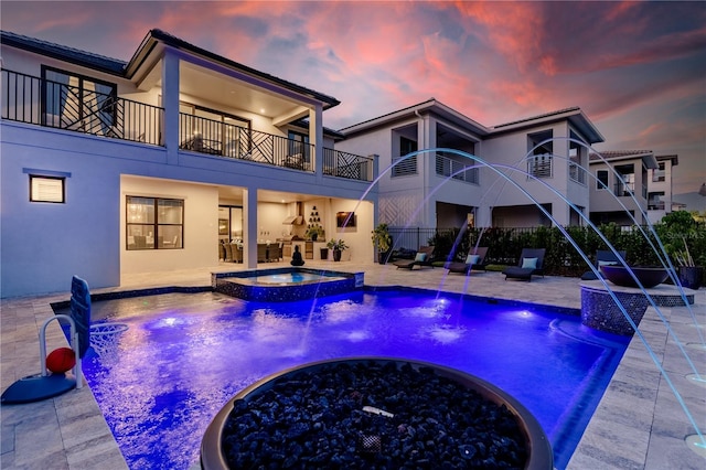 pool at dusk with a patio area, pool water feature, and an in ground hot tub