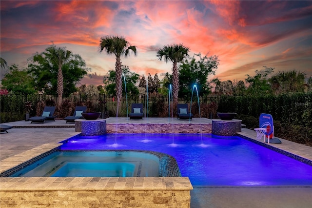 pool at dusk featuring an in ground hot tub, pool water feature, and a patio area