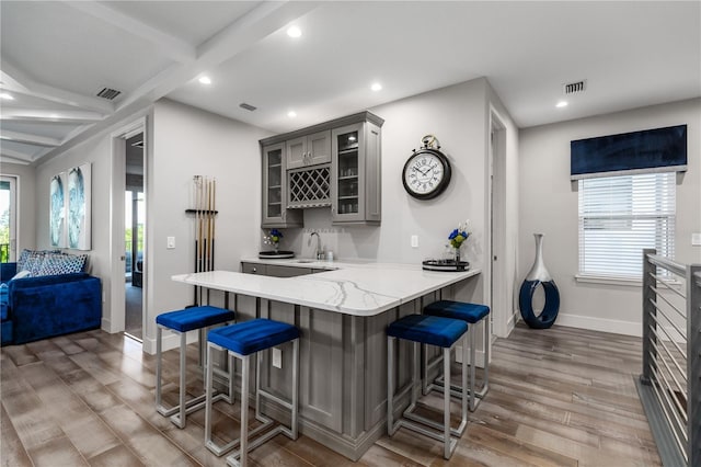 kitchen featuring a breakfast bar area, wood-type flooring, gray cabinets, kitchen peninsula, and a wealth of natural light