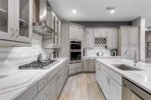 kitchen featuring light stone counters, wall chimney range hood, stainless steel appliances, and sink