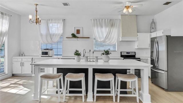 kitchen with stainless steel appliances, white cabinetry, premium range hood, and a center island with sink