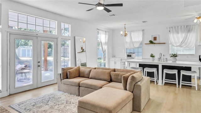 living room featuring ceiling fan with notable chandelier, sink, light hardwood / wood-style flooring, and french doors