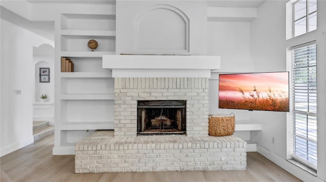 living room with plenty of natural light, light wood-type flooring, built in features, and a fireplace