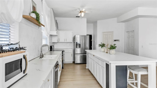 kitchen with sink, white cabinetry, backsplash, stainless steel appliances, and a center island