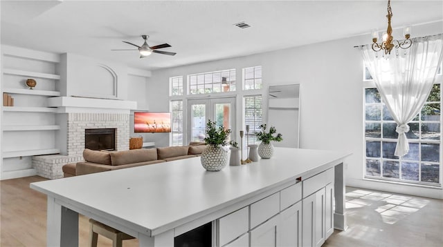 kitchen with built in features, white cabinets, hanging light fixtures, light hardwood / wood-style floors, and a brick fireplace