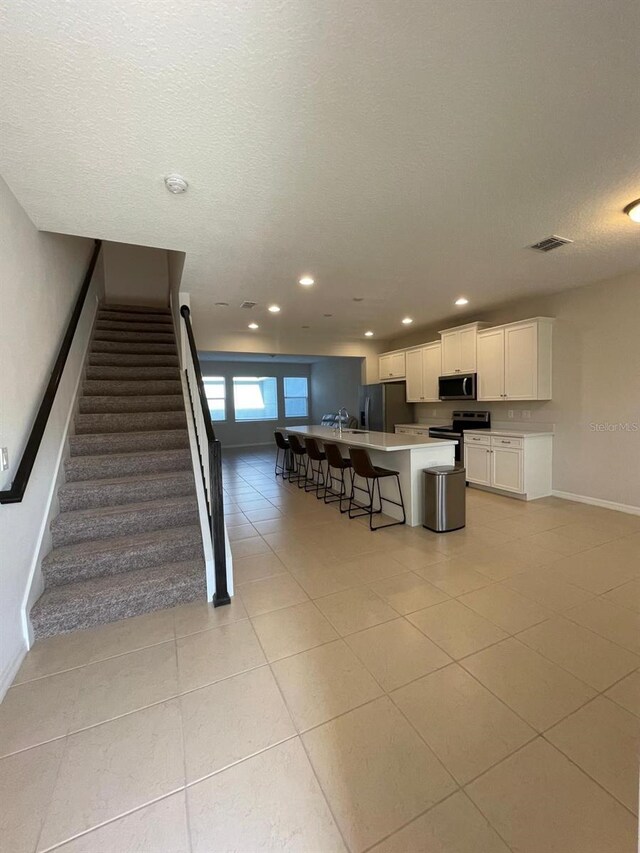 kitchen with light tile patterned floors, a breakfast bar area, appliances with stainless steel finishes, white cabinets, and a kitchen island