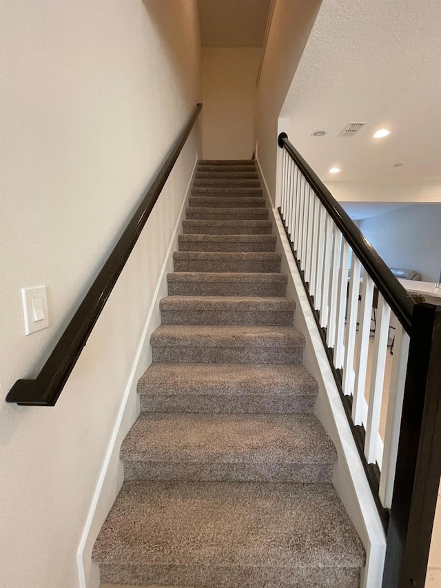 staircase featuring a textured ceiling and carpet