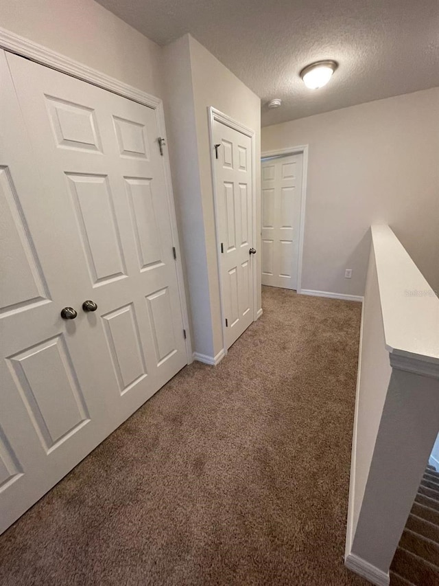 corridor featuring dark carpet and a textured ceiling