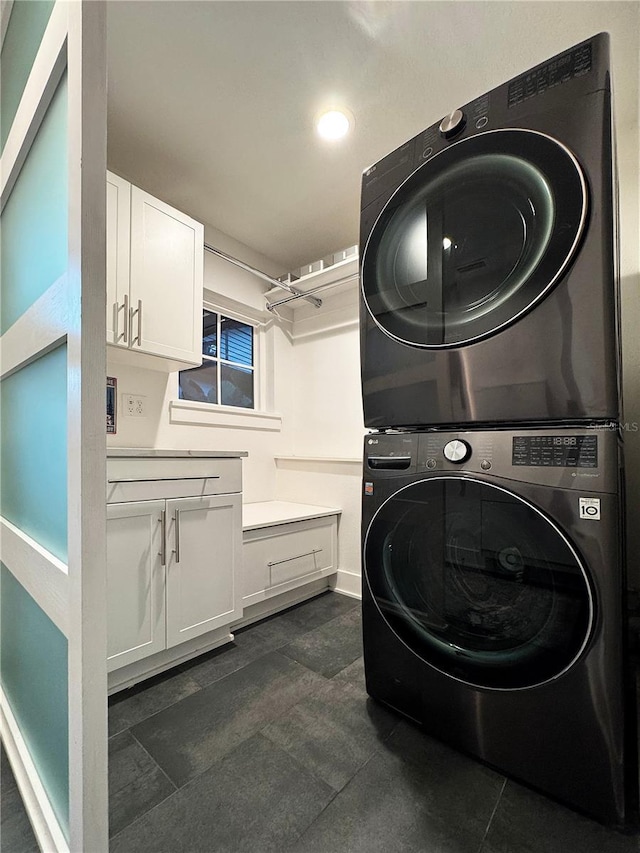 clothes washing area featuring cabinets and stacked washing maching and dryer