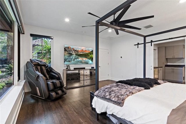 bedroom with ceiling fan, a barn door, and dark hardwood / wood-style flooring