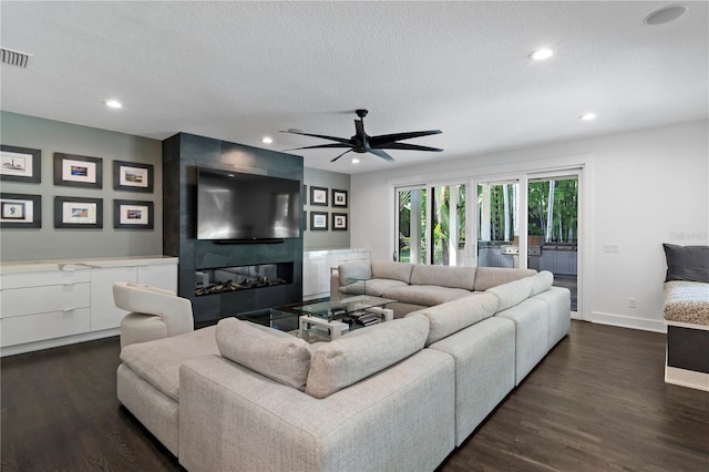 living room with ceiling fan, dark hardwood / wood-style floors, a large fireplace, and a textured ceiling