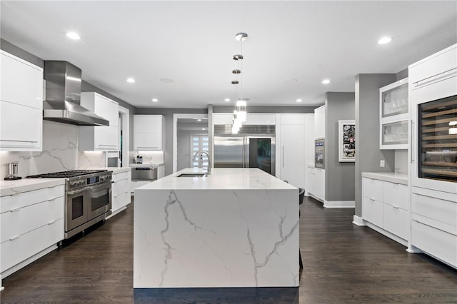 kitchen featuring wall chimney exhaust hood, sink, hanging light fixtures, high quality appliances, and a kitchen island with sink