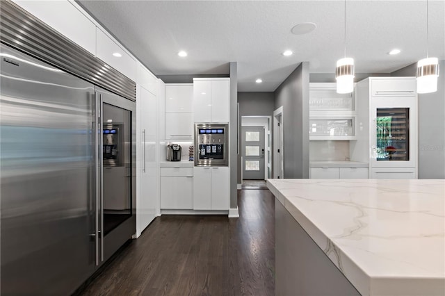 kitchen featuring dark wood-type flooring, white cabinetry, decorative light fixtures, stainless steel appliances, and light stone countertops