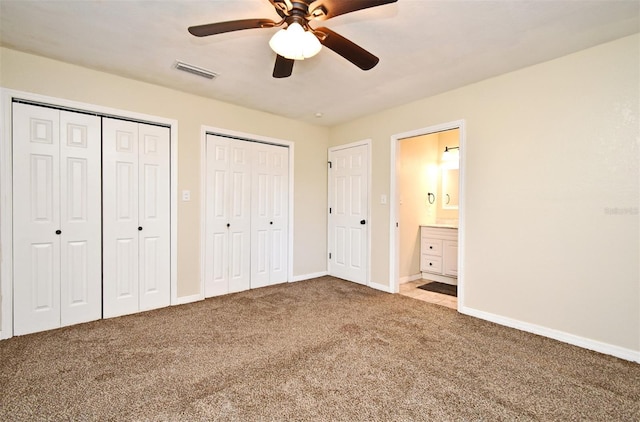 unfurnished bedroom with ceiling fan, connected bathroom, carpet floors, and two closets