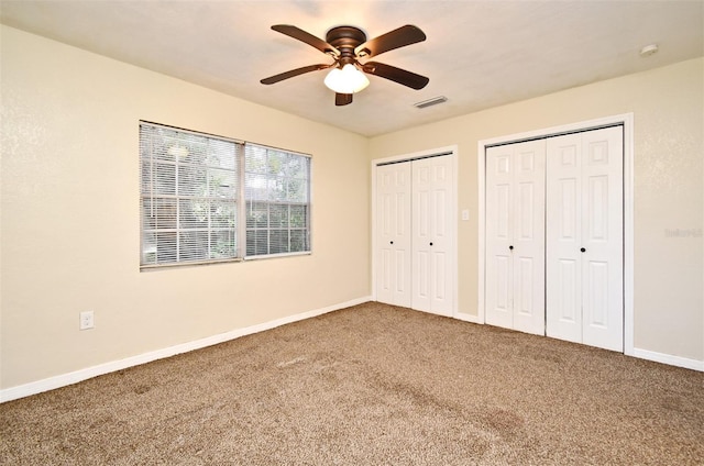 unfurnished bedroom featuring ceiling fan, carpet, and two closets