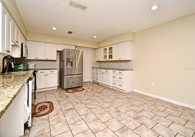 kitchen with light stone counters, white cabinetry, appliances with stainless steel finishes, and backsplash