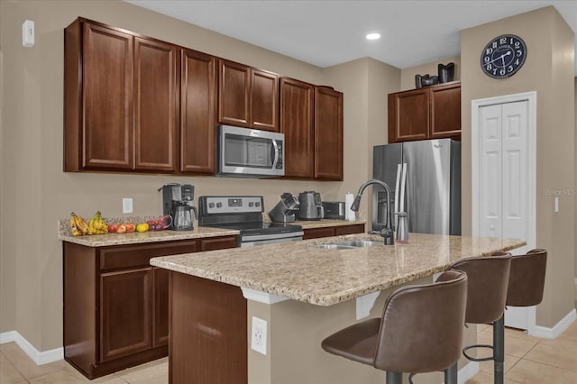 kitchen with light tile patterned flooring, sink, appliances with stainless steel finishes, a kitchen breakfast bar, and a kitchen island with sink