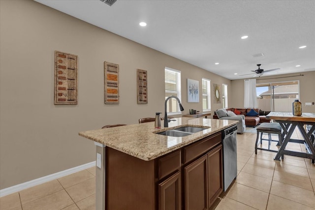 kitchen with sink, dishwasher, light stone counters, an island with sink, and light tile patterned flooring