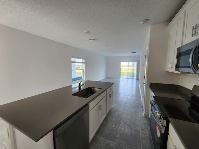 kitchen featuring appliances with stainless steel finishes, sink, white cabinets, dark tile patterned floors, and a center island with sink