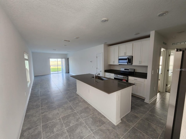 kitchen featuring sink, a textured ceiling, appliances with stainless steel finishes, a kitchen island with sink, and white cabinets