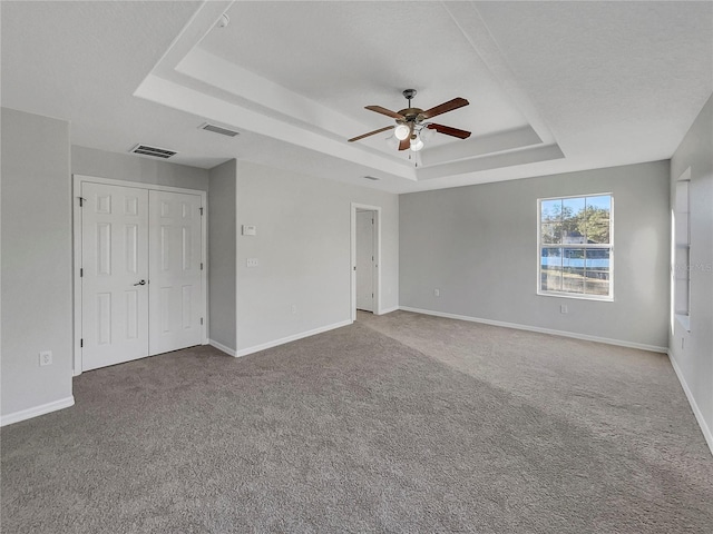 unfurnished bedroom with ceiling fan, a raised ceiling, a textured ceiling, and carpet flooring