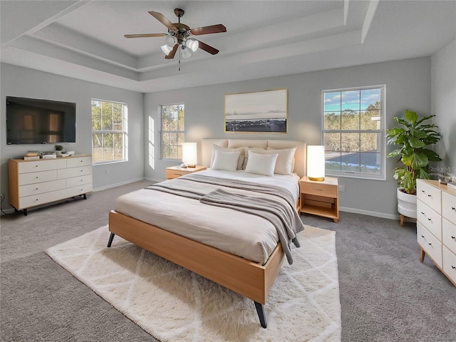 bedroom featuring multiple windows, a tray ceiling, light colored carpet, and ceiling fan