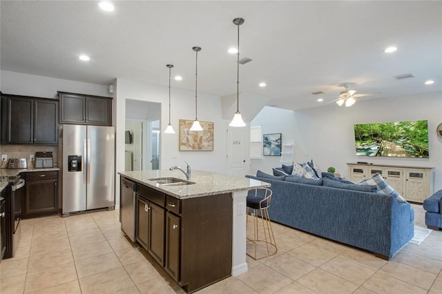 kitchen featuring pendant lighting, sink, a kitchen island with sink, light stone counters, and stainless steel appliances