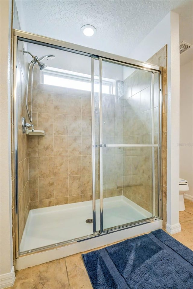 bathroom with a shower with door, tile patterned flooring, a textured ceiling, and toilet