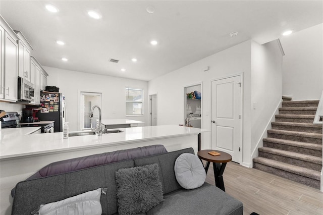 kitchen with sink, white cabinetry, light wood-type flooring, kitchen peninsula, and stainless steel appliances