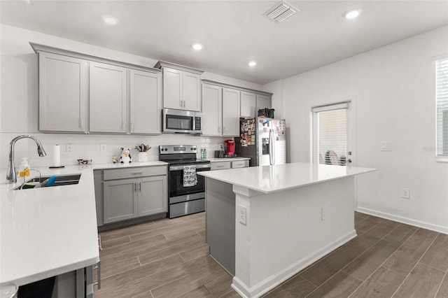 kitchen with appliances with stainless steel finishes, gray cabinets, a center island, and sink