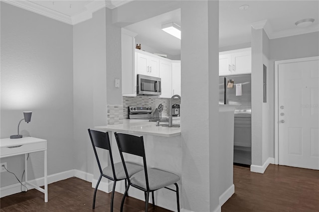 kitchen with white cabinets, a kitchen breakfast bar, decorative backsplash, stainless steel appliances, and crown molding