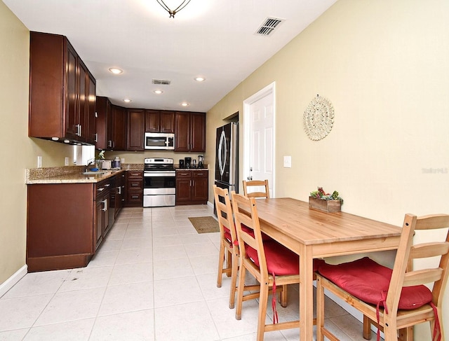 kitchen featuring appliances with stainless steel finishes, sink, light tile patterned floors, light stone countertops, and dark brown cabinets