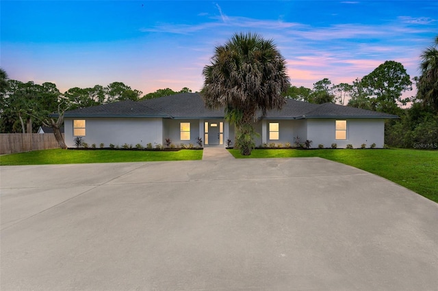 ranch-style home with driveway, a front lawn, fence, and stucco siding