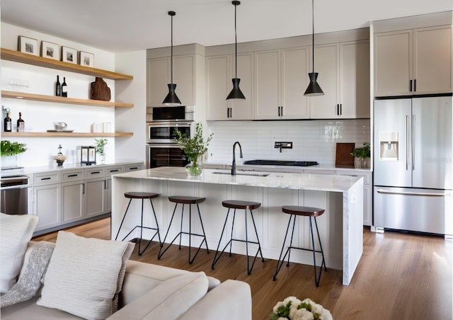 kitchen with tasteful backsplash, a sink, appliances with stainless steel finishes, a kitchen breakfast bar, and open shelves