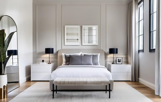 bedroom with baseboards, multiple windows, a decorative wall, and light wood finished floors