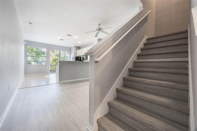 staircase featuring hardwood / wood-style flooring, ceiling fan, and a textured ceiling