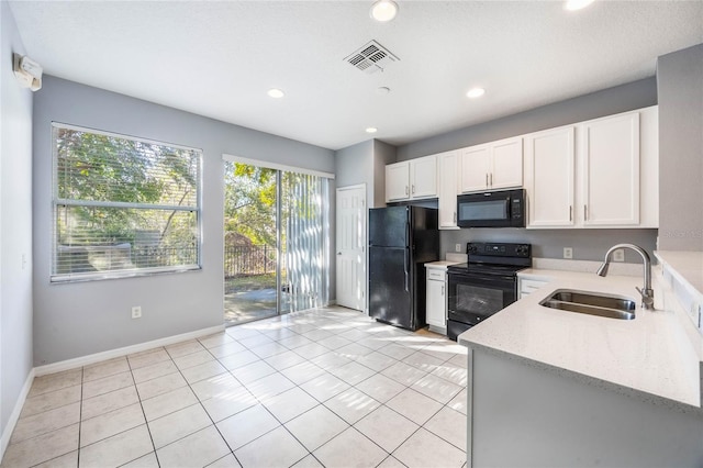 kitchen with sink, black appliances, light tile patterned floors, light stone countertops, and white cabinets