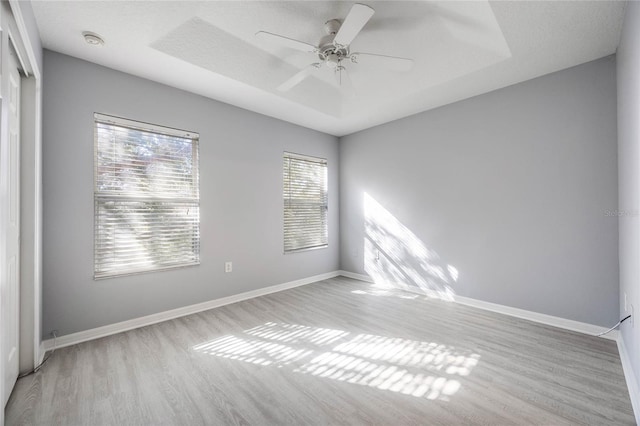 spare room featuring a raised ceiling, ceiling fan, and light hardwood / wood-style flooring