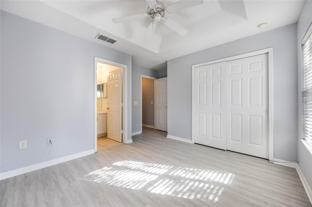 unfurnished bedroom featuring ensuite bathroom, a tray ceiling, a closet, and light wood-type flooring