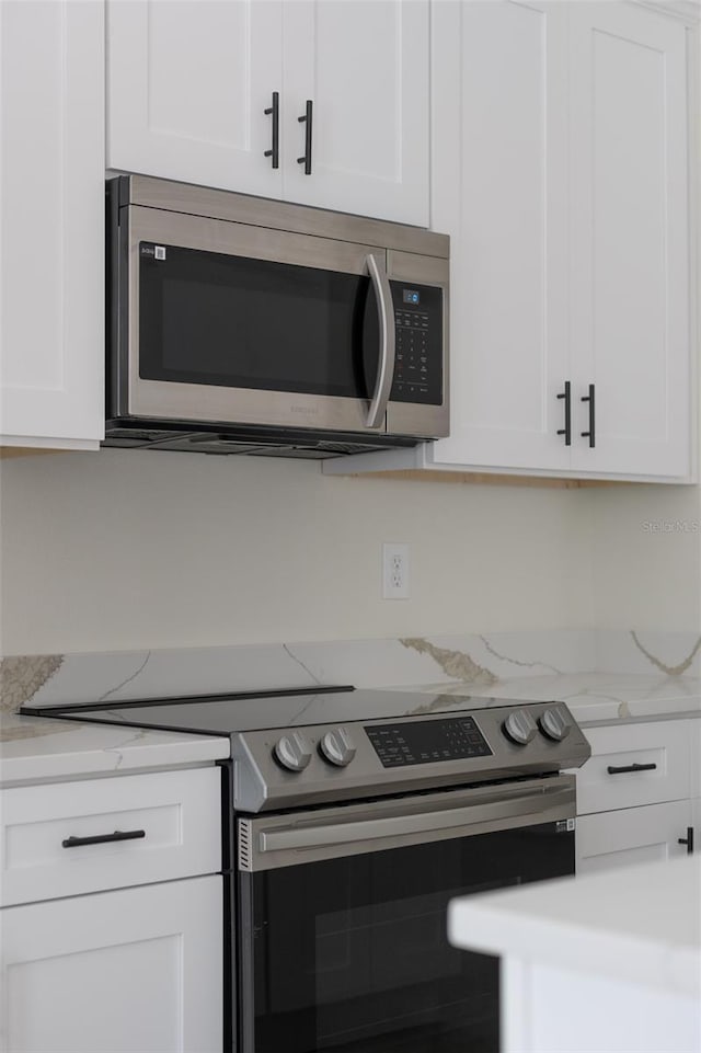 kitchen featuring stainless steel appliances, light stone countertops, and white cabinets