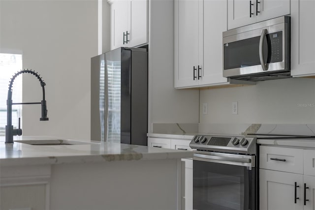 kitchen with light stone counters, stainless steel appliances, sink, and white cabinets