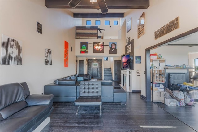 living room with beamed ceiling, dark hardwood / wood-style floors, ceiling fan, and a towering ceiling