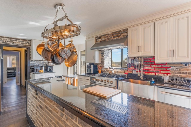 kitchen with tasteful backsplash, high end stainless steel range oven, dark stone counters, cream cabinets, and wall chimney range hood