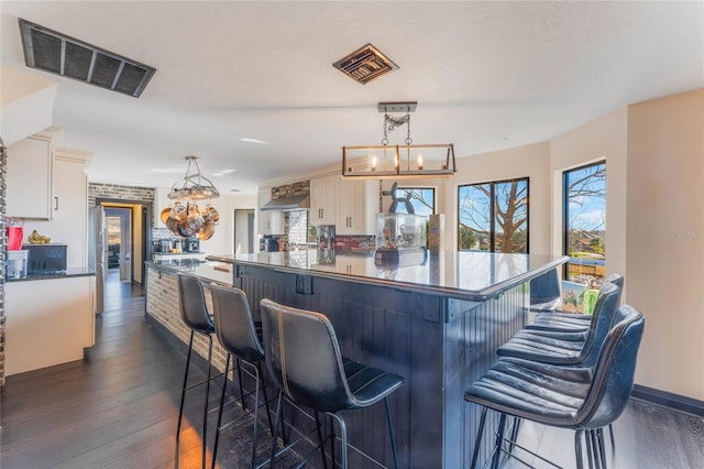 kitchen featuring wall chimney range hood, decorative light fixtures, stainless steel fridge, and a kitchen breakfast bar