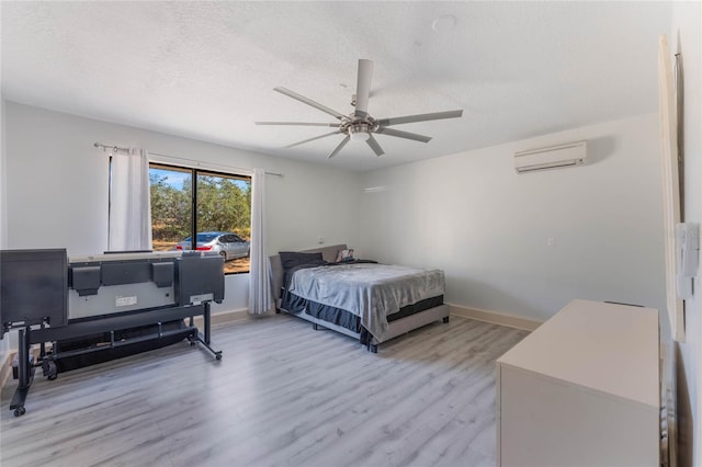 bedroom with ceiling fan, a textured ceiling, light hardwood / wood-style flooring, and a wall mounted AC