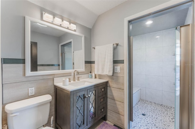 bathroom with vanity, a tile shower, tile walls, and toilet