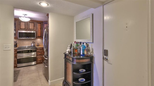 kitchen with appliances with stainless steel finishes, a textured ceiling, decorative backsplash, and light tile patterned floors